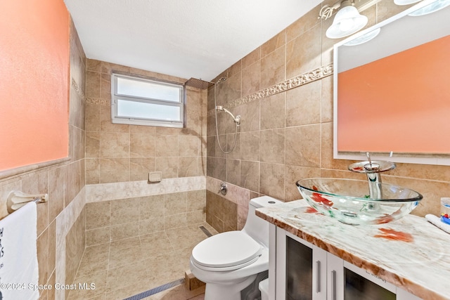 bathroom with a tile shower, vanity, toilet, and tile walls