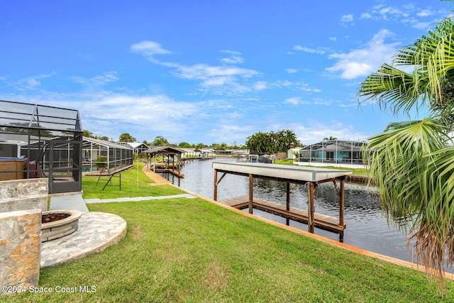 view of dock with a yard, a water view, glass enclosure, and an outdoor fire pit