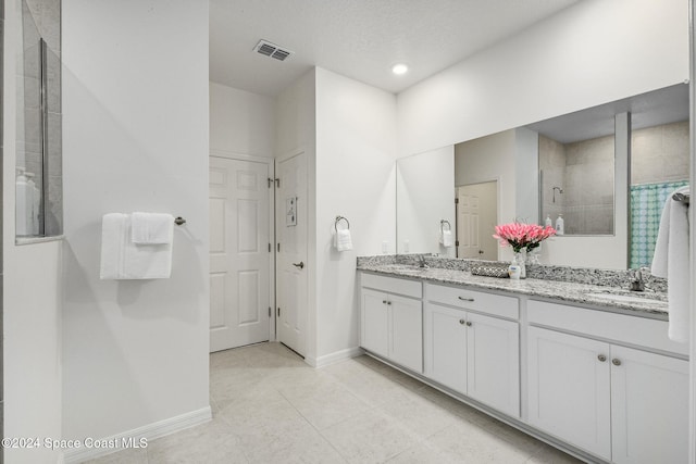 bathroom featuring tile patterned flooring, vanity, a textured ceiling, and a tile shower