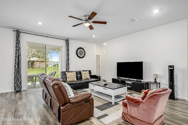 living room with a textured ceiling, light wood-type flooring, and ceiling fan