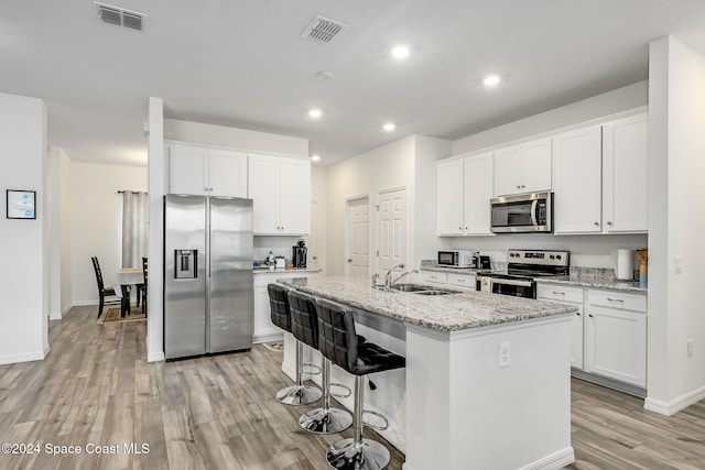 kitchen featuring stainless steel appliances, white cabinetry, light stone countertops, sink, and an island with sink