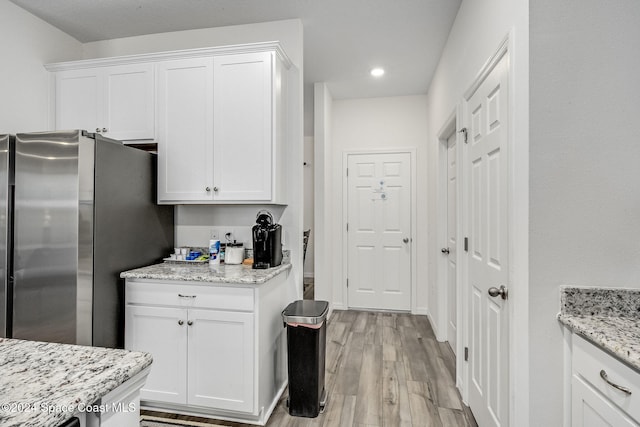 kitchen featuring white cabinets, light hardwood / wood-style flooring, stainless steel refrigerator, and light stone countertops