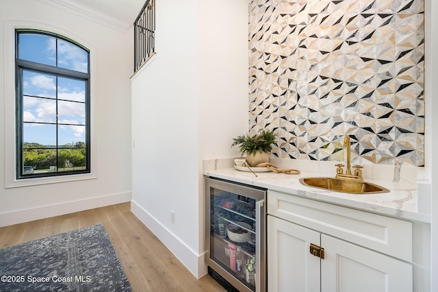 bar with white cabinets, beverage cooler, crown molding, light stone countertops, and light hardwood / wood-style flooring