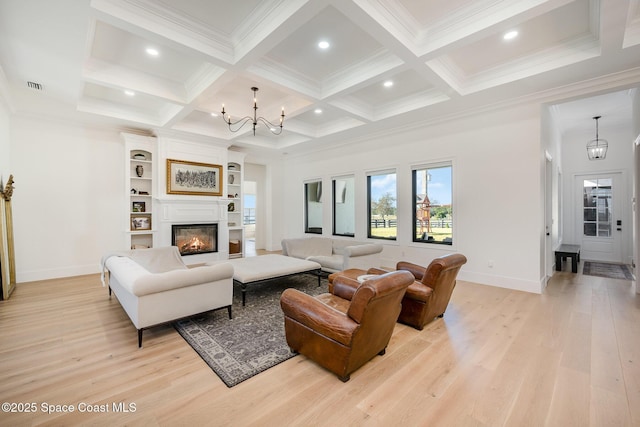 living room with beamed ceiling, ornamental molding, an inviting chandelier, and light hardwood / wood-style flooring