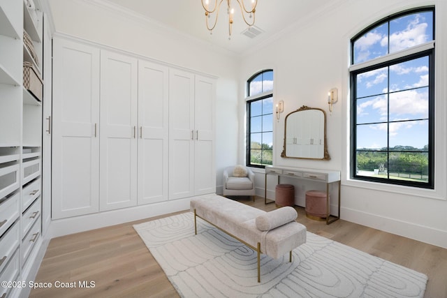 living area with crown molding, a notable chandelier, and light wood-type flooring