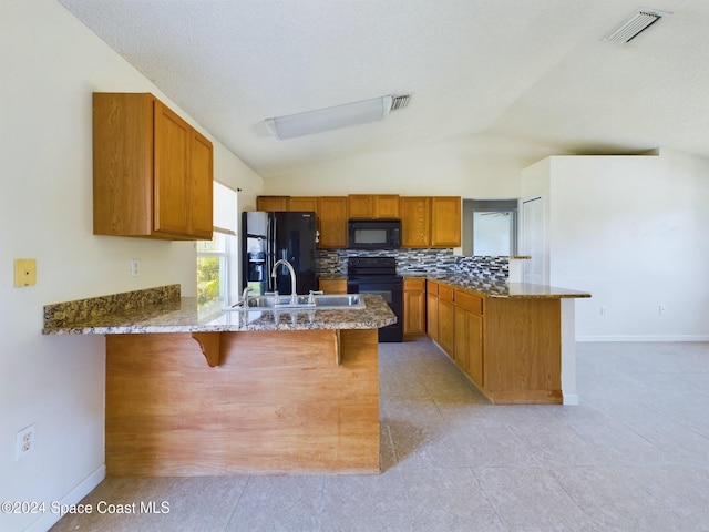 kitchen featuring black appliances, kitchen peninsula, vaulted ceiling, and a kitchen breakfast bar