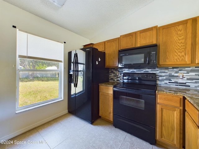 kitchen featuring black appliances, tasteful backsplash, dark stone counters, light tile patterned floors, and vaulted ceiling