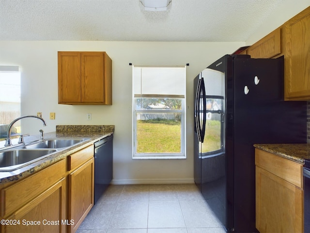 kitchen with black appliances, light tile patterned flooring, a textured ceiling, sink, and dark stone countertops