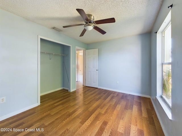 unfurnished bedroom with a closet, hardwood / wood-style floors, ceiling fan, and a textured ceiling