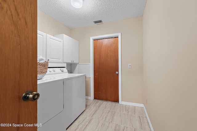 clothes washing area featuring cabinets, a textured ceiling, and washer and dryer