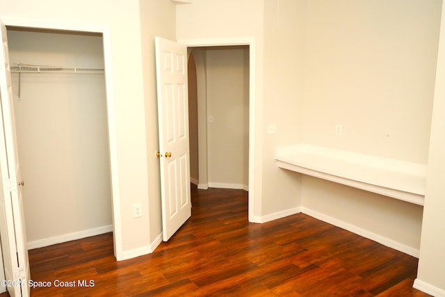 unfurnished bedroom with dark wood-type flooring, a closet, and baseboards