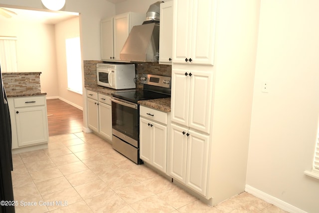 kitchen with tasteful backsplash, electric range, white microwave, wall chimney range hood, and dark stone counters