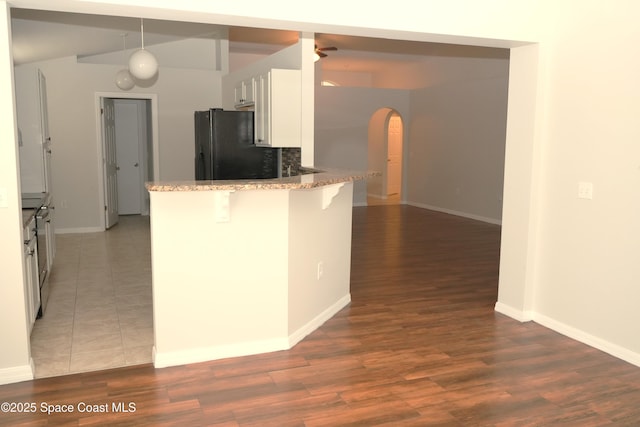 kitchen featuring white cabinets, light stone counters, freestanding refrigerator, a peninsula, and a kitchen bar