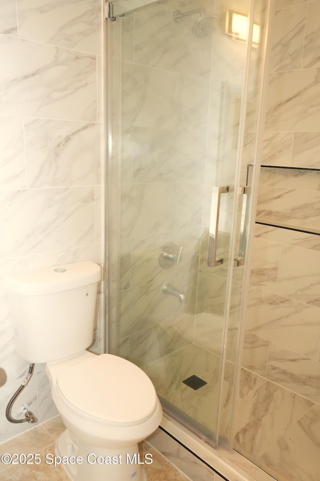 bathroom featuring toilet, a shower stall, and tile walls