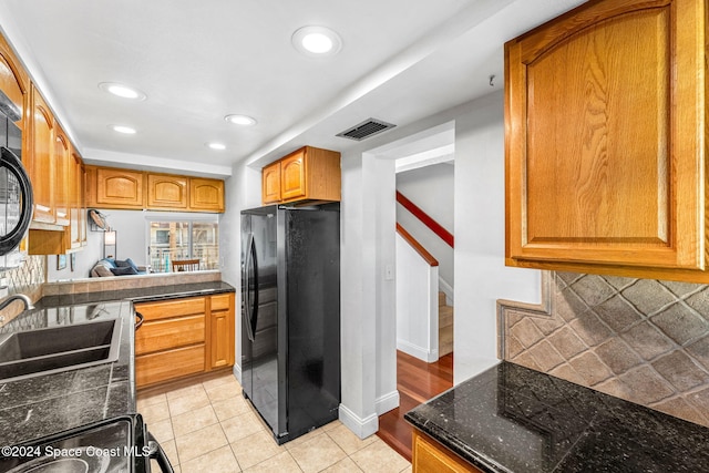 kitchen with tasteful backsplash, black fridge, sink, and light tile patterned flooring