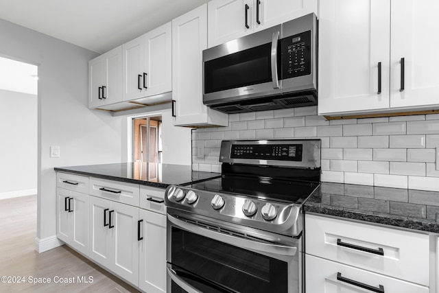 kitchen with white cabinets, appliances with stainless steel finishes, dark stone counters, and backsplash