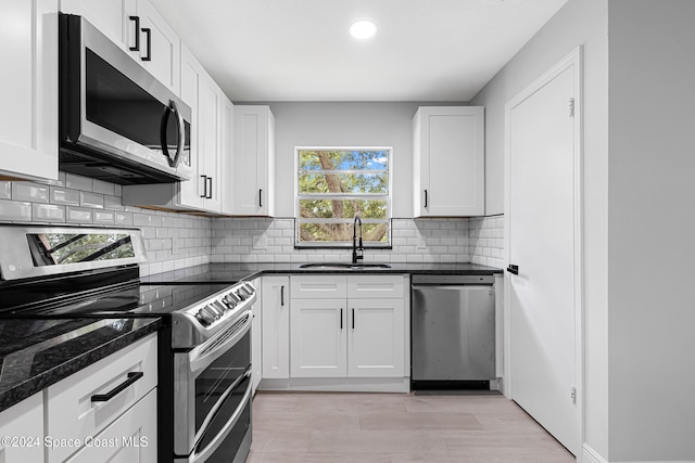 kitchen with stainless steel appliances, white cabinetry, sink, light hardwood / wood-style floors, and dark stone countertops