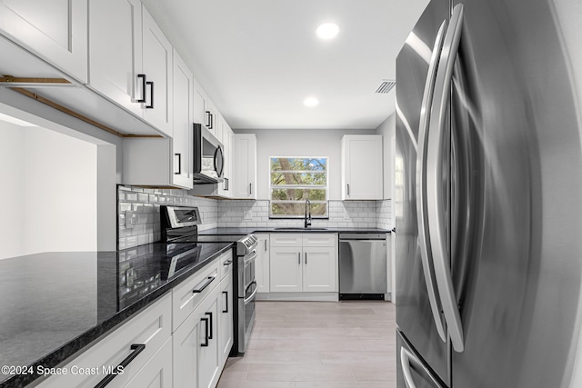 kitchen with appliances with stainless steel finishes, sink, white cabinets, dark stone countertops, and light hardwood / wood-style flooring