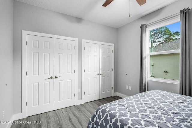 bedroom with light hardwood / wood-style floors, a textured ceiling, two closets, and ceiling fan