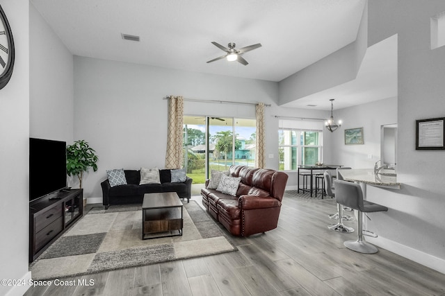 living room with ceiling fan with notable chandelier and light hardwood / wood-style flooring