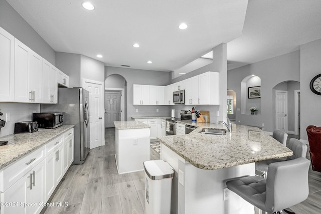 kitchen with appliances with stainless steel finishes, sink, a breakfast bar area, kitchen peninsula, and light hardwood / wood-style flooring