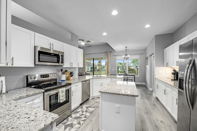 kitchen with stainless steel appliances, white cabinetry, light stone countertops, hanging light fixtures, and a kitchen island