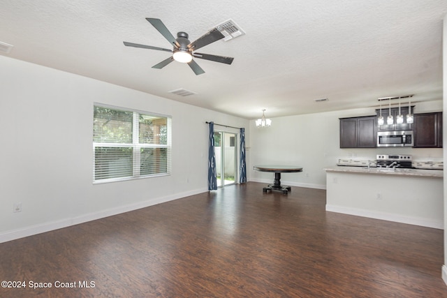 unfurnished living room featuring ceiling fan with notable chandelier, dark hardwood / wood-style flooring, and a textured ceiling