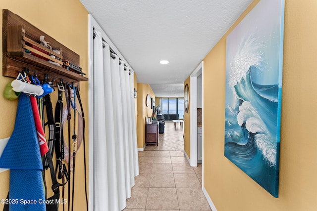 corridor with light tile patterned floors, baseboards, and a textured ceiling