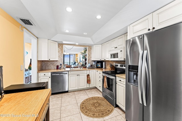 kitchen featuring visible vents, decorative backsplash, light tile patterned flooring, stainless steel appliances, and a raised ceiling