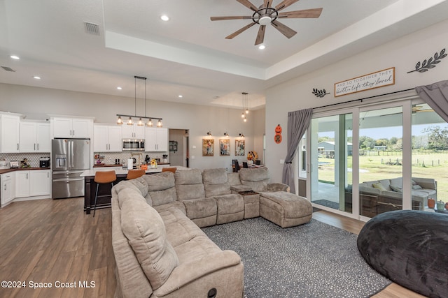 living room with dark hardwood / wood-style flooring, ceiling fan, and a raised ceiling