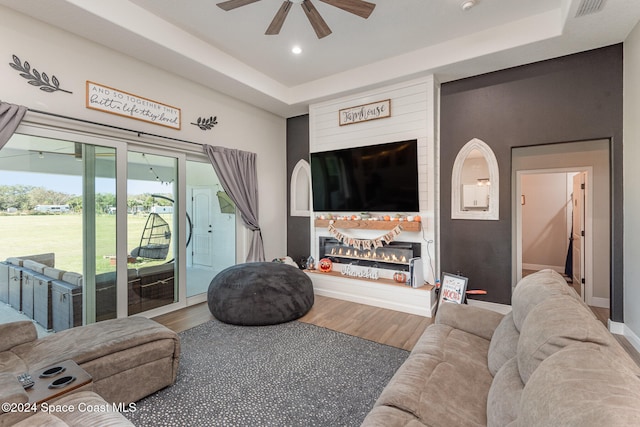 living room with wood-type flooring, a tray ceiling, and ceiling fan