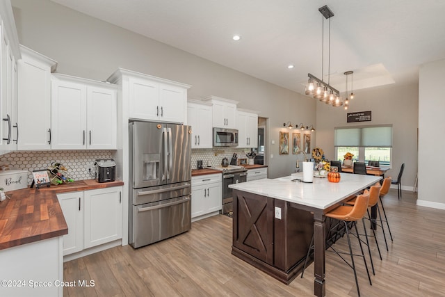 kitchen featuring wood counters, light wood-type flooring, stainless steel appliances, white cabinets, and hanging light fixtures