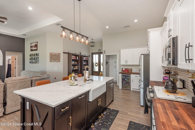 kitchen with hanging light fixtures, beverage cooler, stainless steel appliances, tasteful backsplash, and a center island with sink