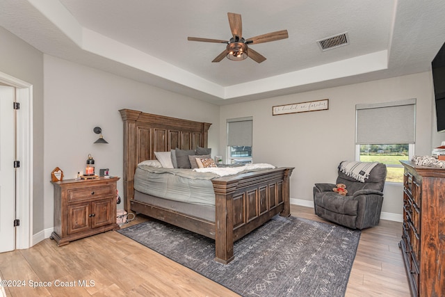 bedroom with a raised ceiling, ceiling fan, wood-type flooring, and a textured ceiling