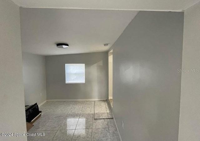 empty room with light tile patterned floors and vaulted ceiling