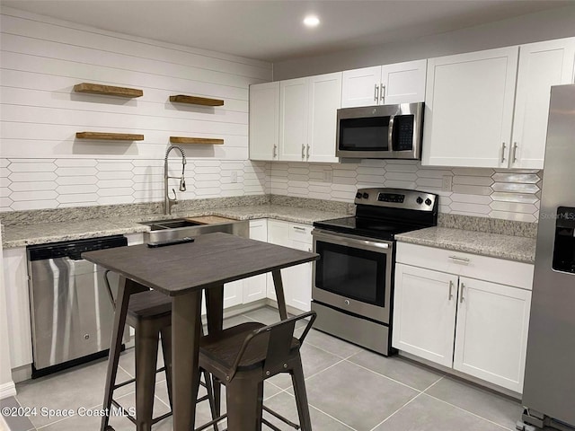 kitchen with white cabinetry, appliances with stainless steel finishes, sink, and light stone counters