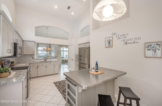 kitchen featuring appliances with stainless steel finishes, gray cabinets, high vaulted ceiling, and a kitchen island