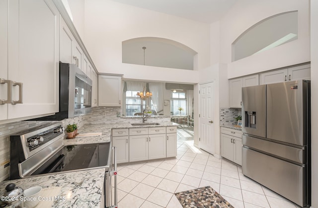 kitchen featuring a towering ceiling, stainless steel appliances, sink, pendant lighting, and light tile patterned floors