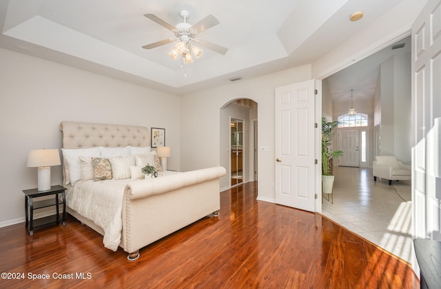 bedroom with a raised ceiling, ceiling fan, and wood-type flooring