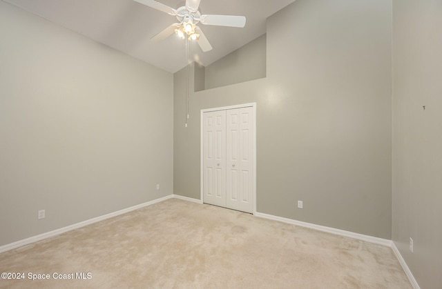 empty room featuring ceiling fan, light colored carpet, and high vaulted ceiling