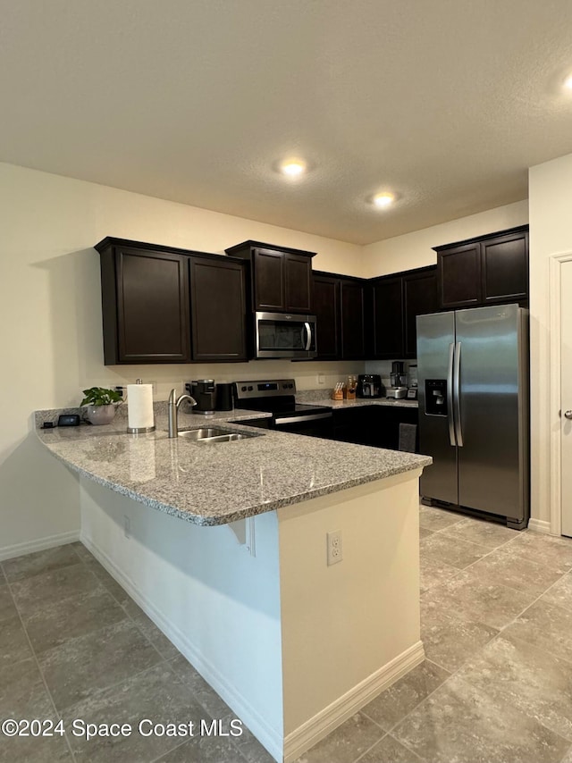 kitchen featuring kitchen peninsula, sink, light stone counters, and appliances with stainless steel finishes