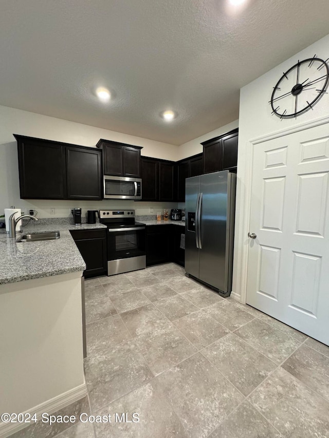 kitchen with a textured ceiling, light stone countertops, sink, and stainless steel appliances