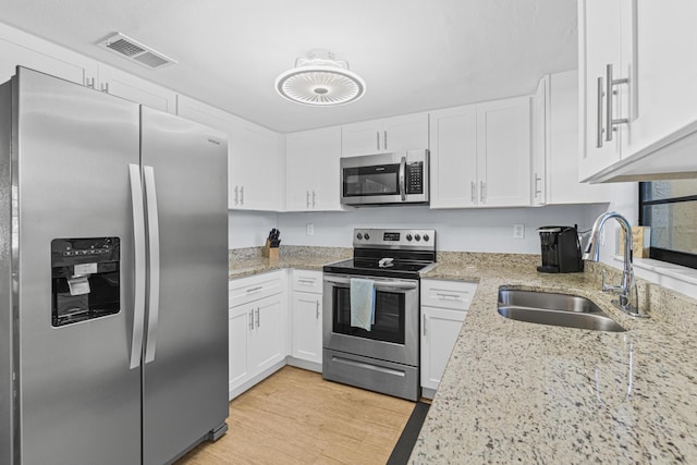 kitchen with sink, light stone countertops, light wood-type flooring, white cabinetry, and stainless steel appliances