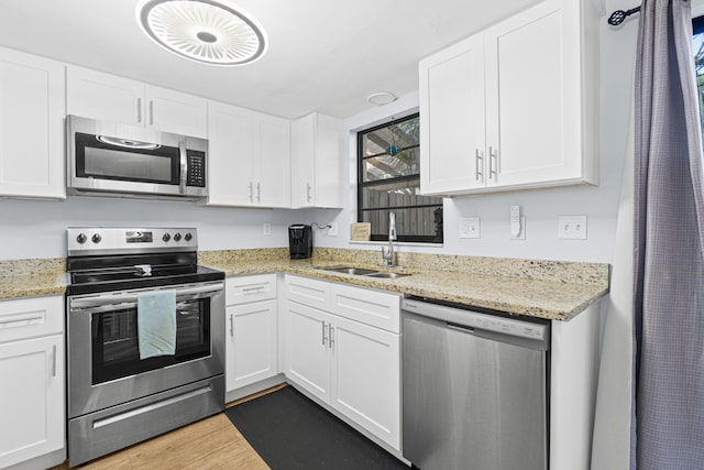 kitchen with light stone countertops, stainless steel appliances, sink, light hardwood / wood-style flooring, and white cabinetry