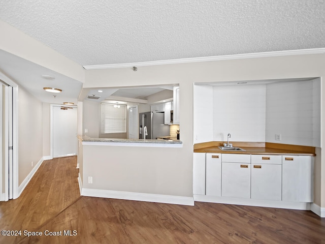 kitchen with hardwood / wood-style flooring, sink, a textured ceiling, white cabinets, and stainless steel fridge