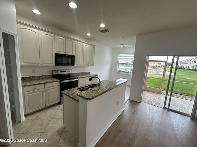 kitchen with sink, white cabinets, dark stone countertops, a kitchen island with sink, and stainless steel range with electric cooktop