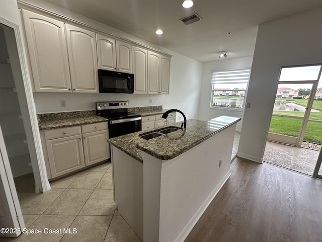 kitchen with stainless steel electric stove, dark stone countertops, a center island with sink, and sink