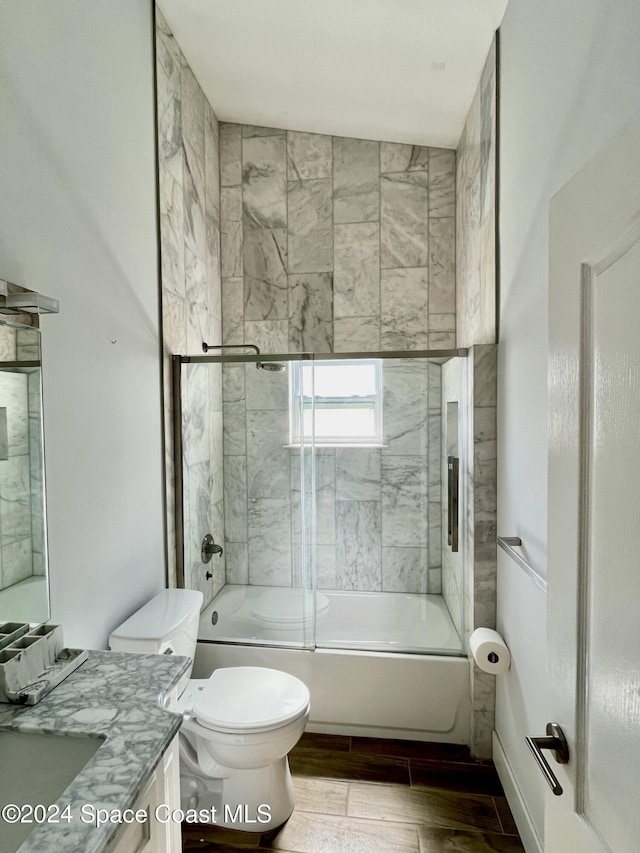 full bathroom with vanity, bath / shower combo with glass door, hardwood / wood-style floors, vaulted ceiling, and toilet