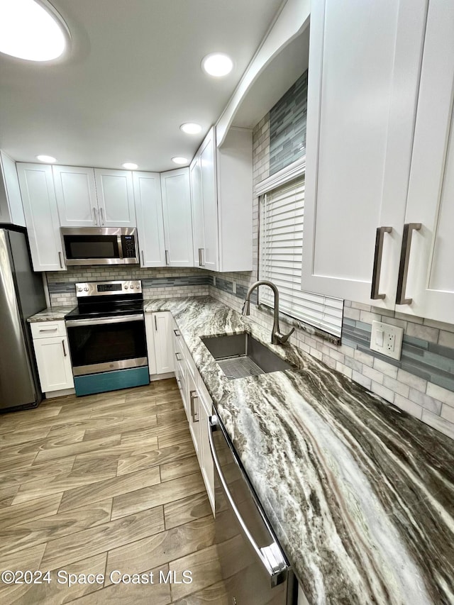 kitchen featuring stainless steel appliances, sink, light stone counters, tasteful backsplash, and white cabinets