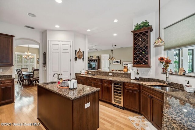 kitchen with a center island, light hardwood / wood-style flooring, dark stone countertops, decorative light fixtures, and beverage cooler